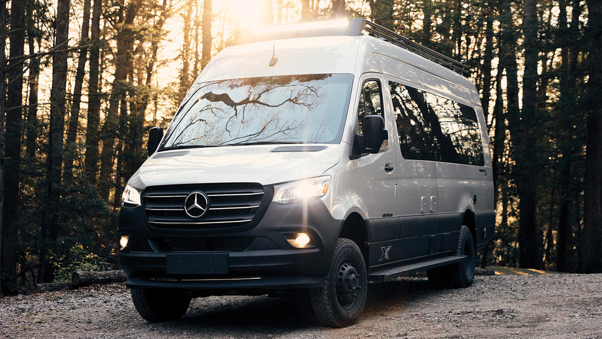 Explore nature with this Mercedes Sprinter camper van RV rental, parked on a dirt road in a sunlit forest. Off-road adventure.