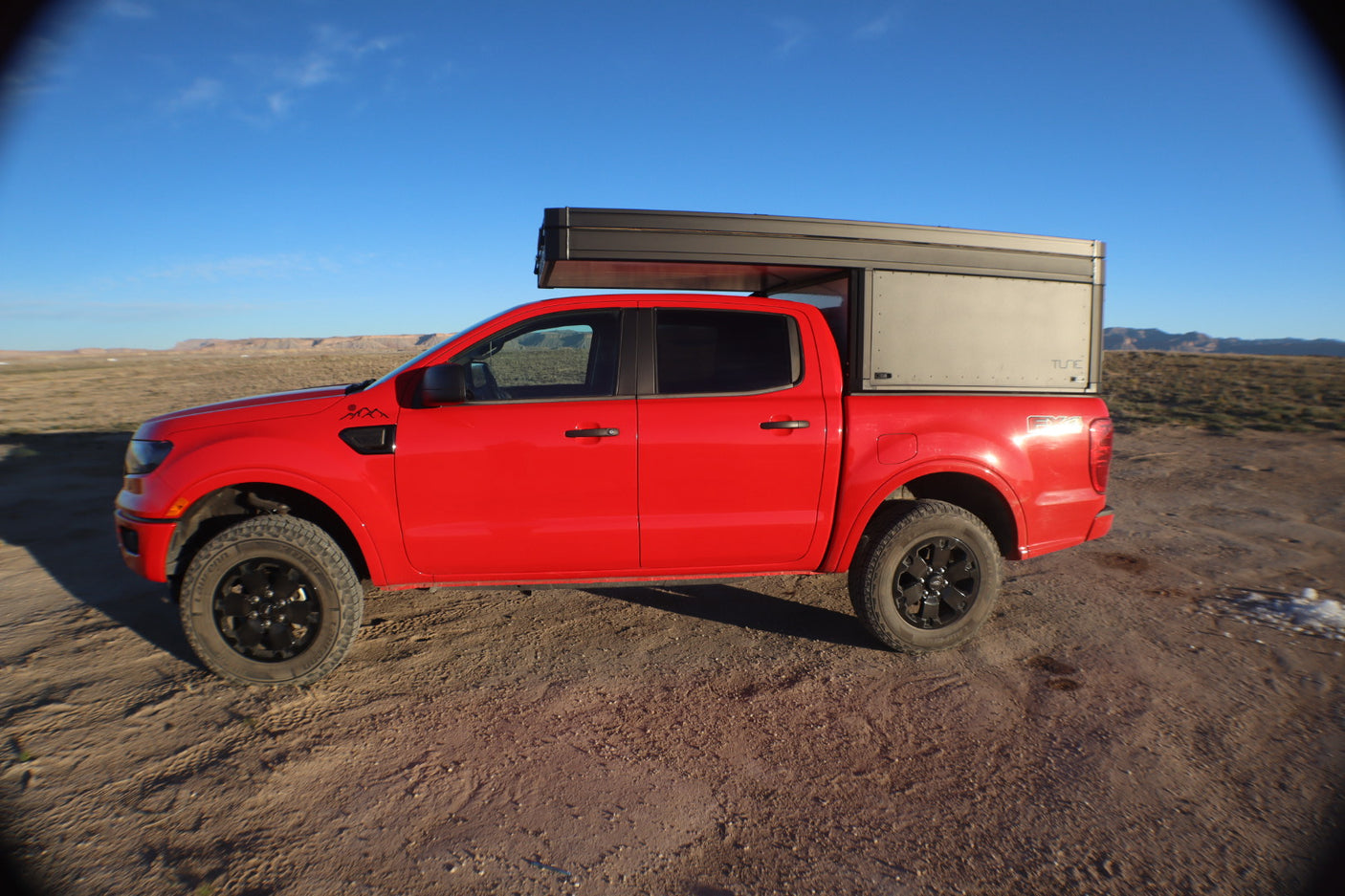 Red Ford Ranger pickup truck with a Tune camper, parked in a desert landscape. Perfect overland rv rental for off-road adventures.