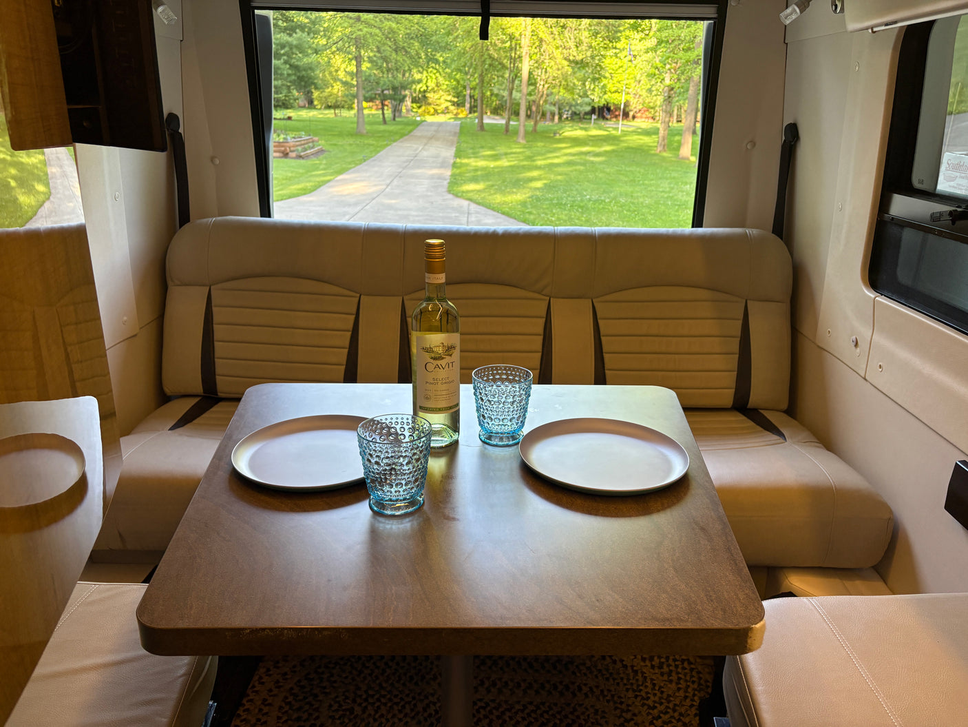 Relaxing rv rental interior: dinette with wine, glasses, plates, and a green outdoor view through the large window.