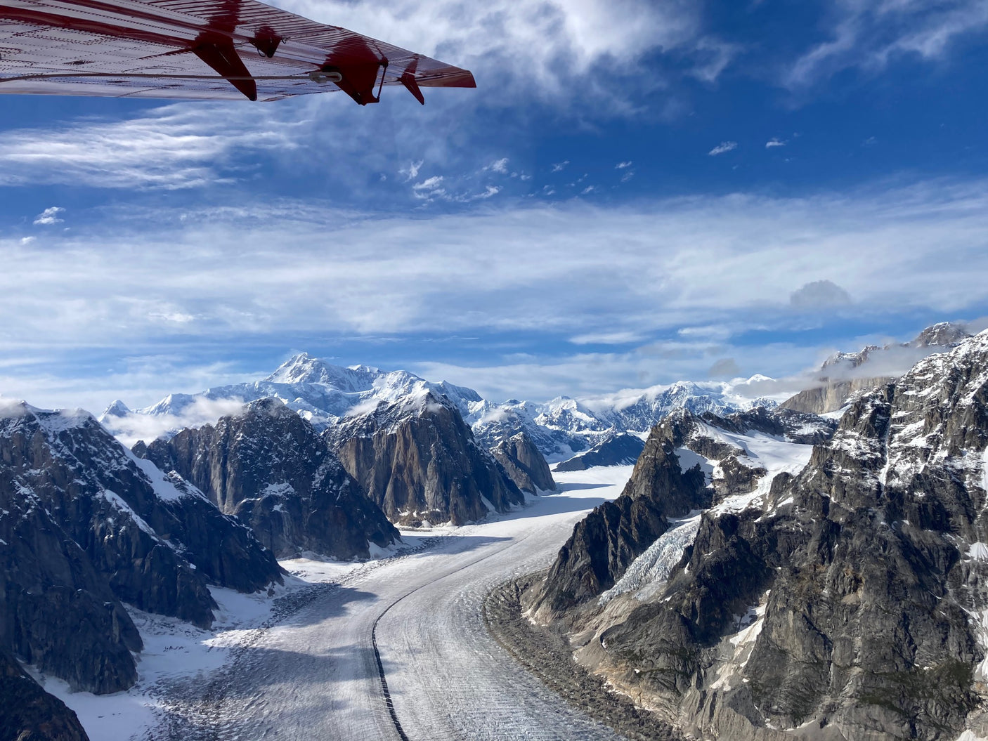 Aerial view: A red airplane wing overlooks vast glaciers winding through snow-capped mountains. Perfect for an RV rental adventure.