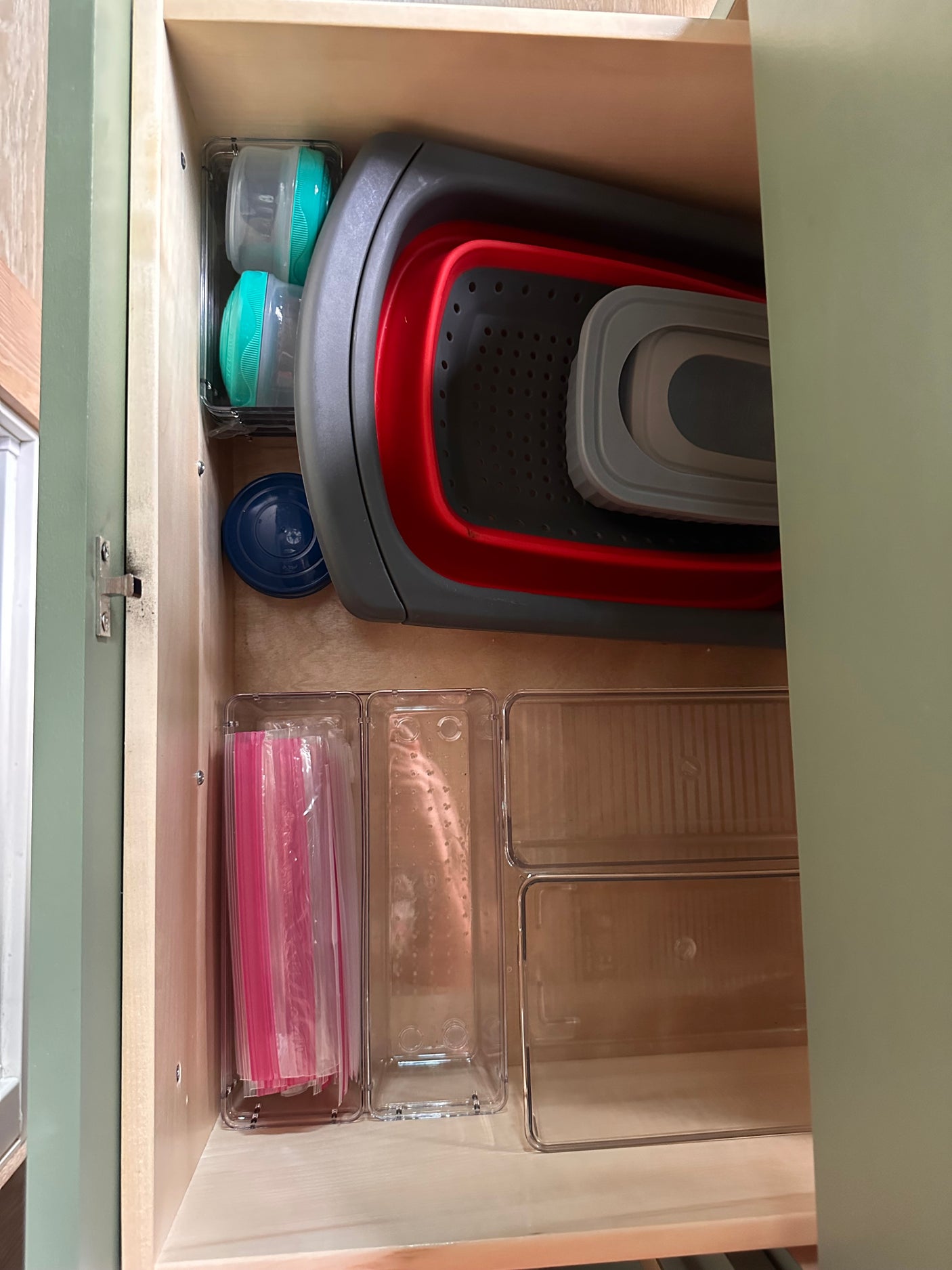 Optimized drawer storage in an RV rental kitchen, with clear bins, a collapsible strainer, and baby containers.