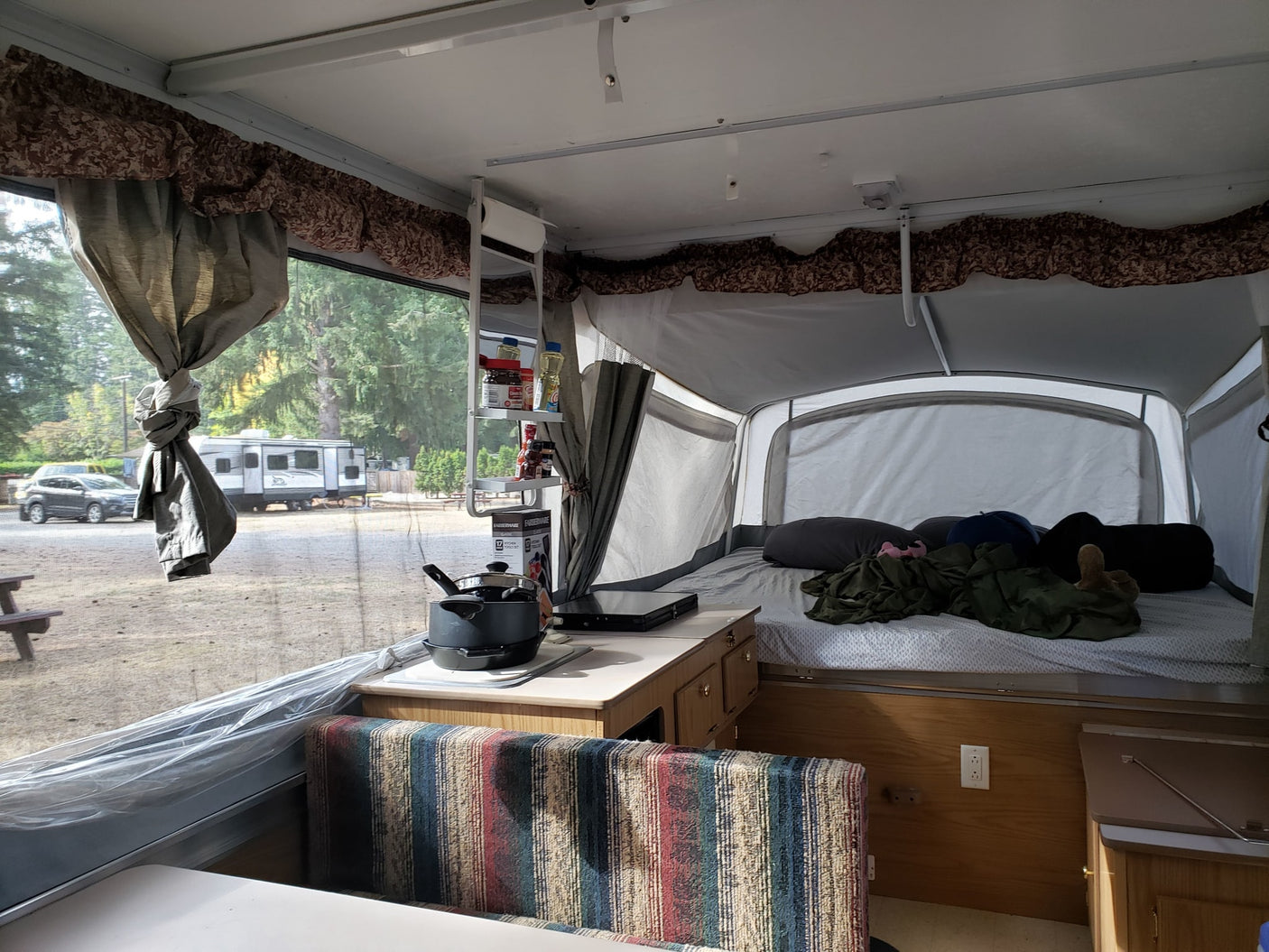 parked under a sunny tree for your next outdoor adventure.|A black SUV and pop-up RV rental are set up for a sunny day camping in a lush forest campsite.|Cozy pop-up camper rv rental interior