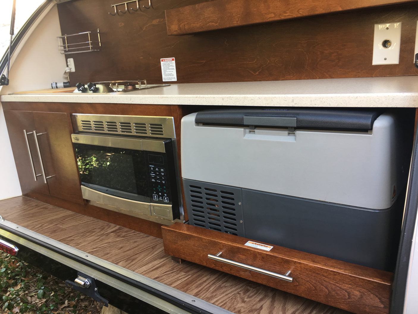Explore this RV rental's equipped outdoor kitchen: microwave, portable fridge, sink, and storage cabinets for your travels.