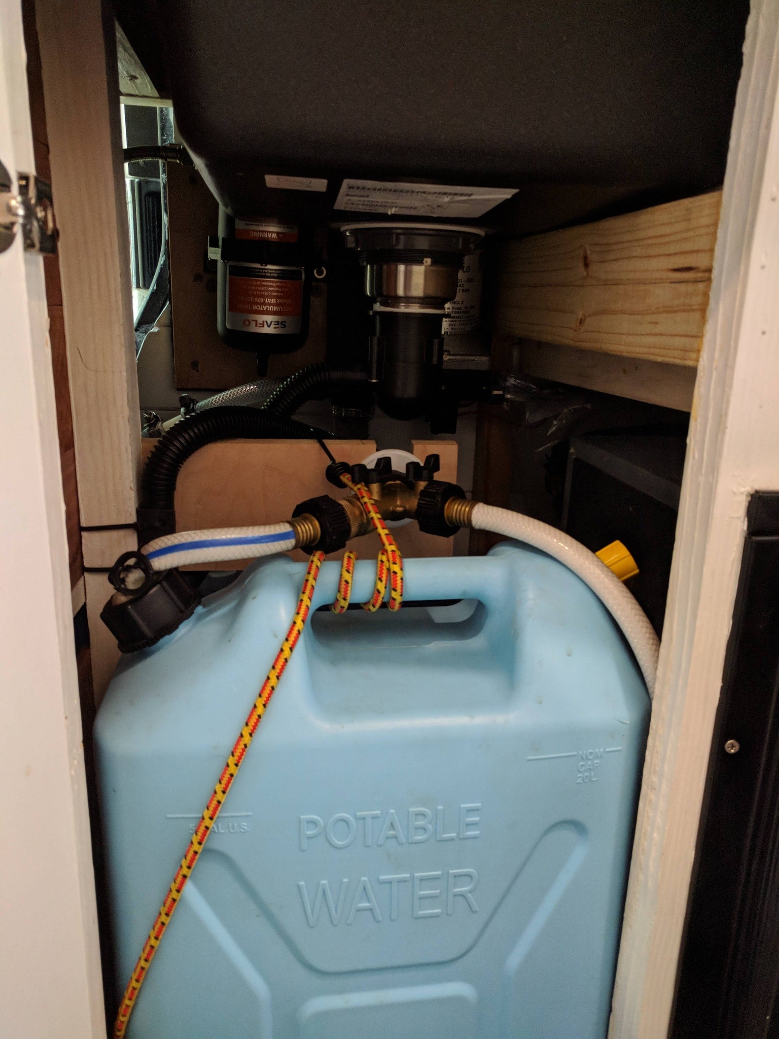 RV rental water system: A light blue potable water jug, hoses, and SEAFLO accumulator tank are installed under a sink.