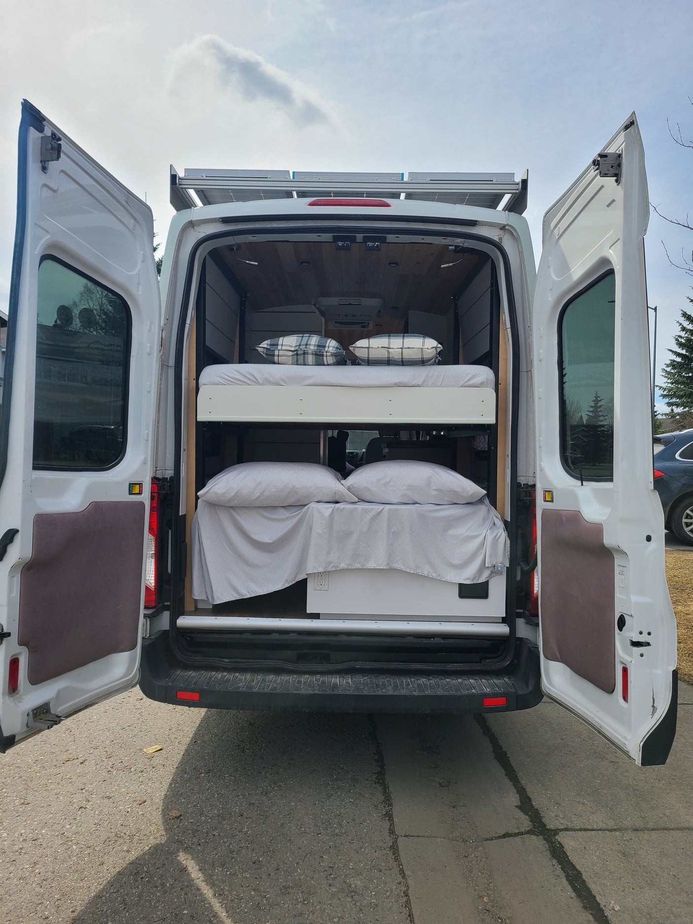 Open rear doors of an RV rental camper van reveal bunk beds, wood paneling, and solar panels on top.
