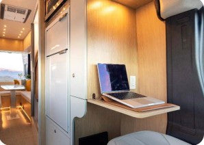 This rv rental features a well-lit mobile office with a laptop on a sleek wooden desk, perfect for remote work on the go.