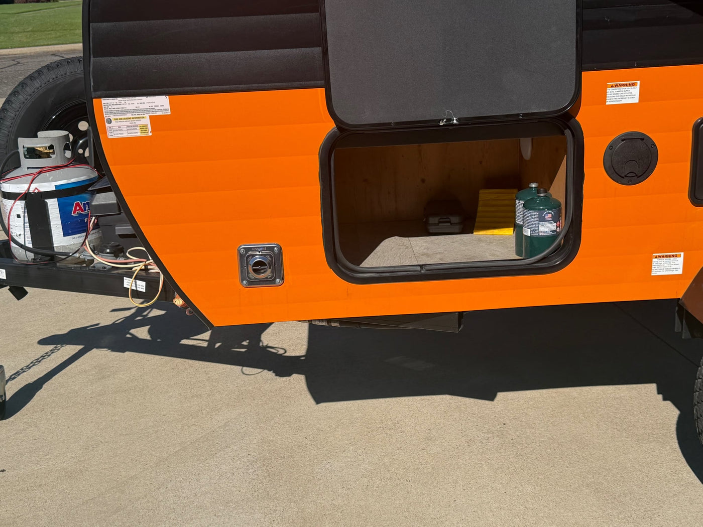 and warning sticker on the orange side panel.|Orange rv rental side showing an open storage compartment with gear — photo 6