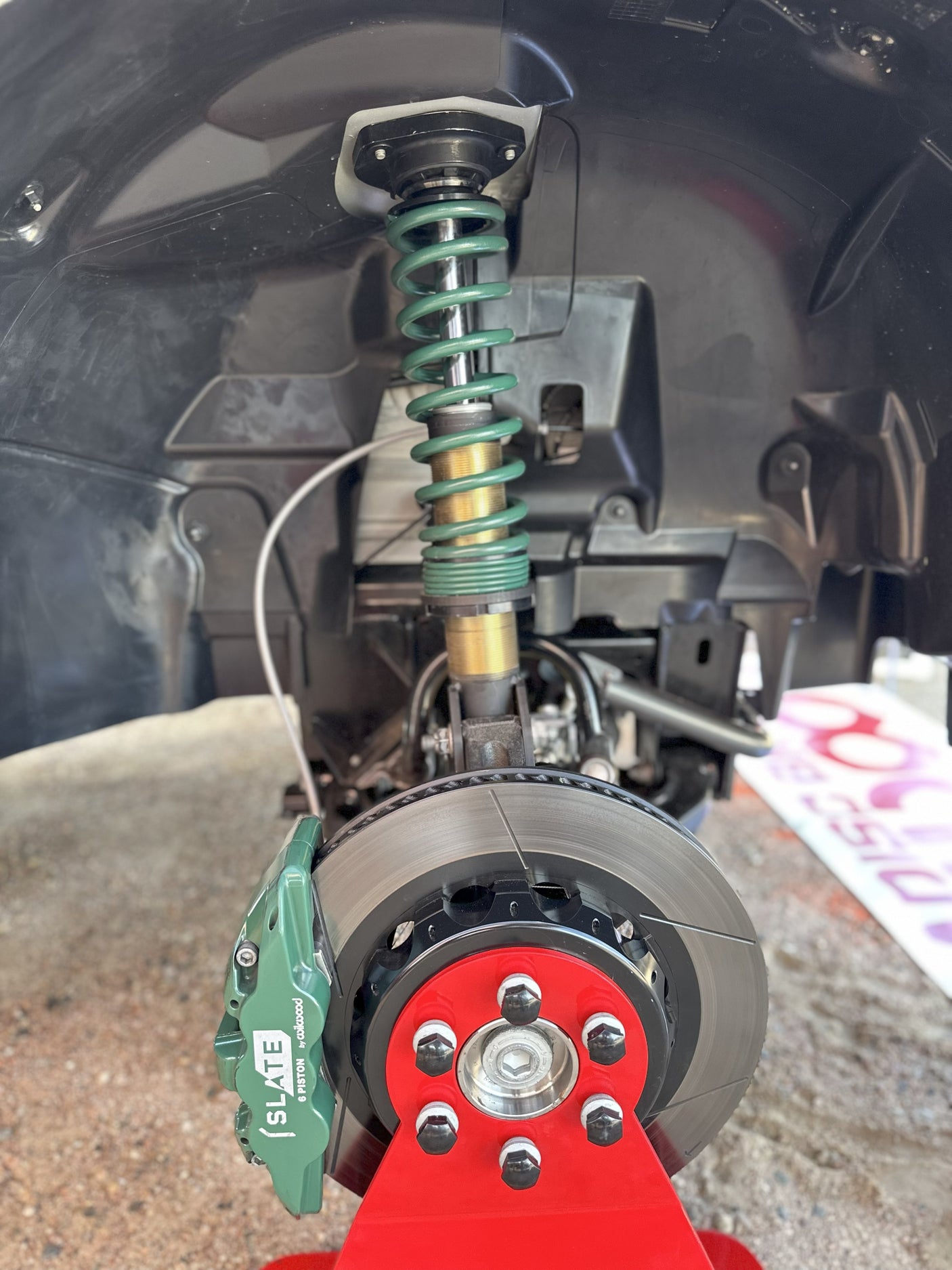 Close-up of a car's green Slate 6-piston brake caliper, rotor & coilover suspension. Much different than an RV rental setup.