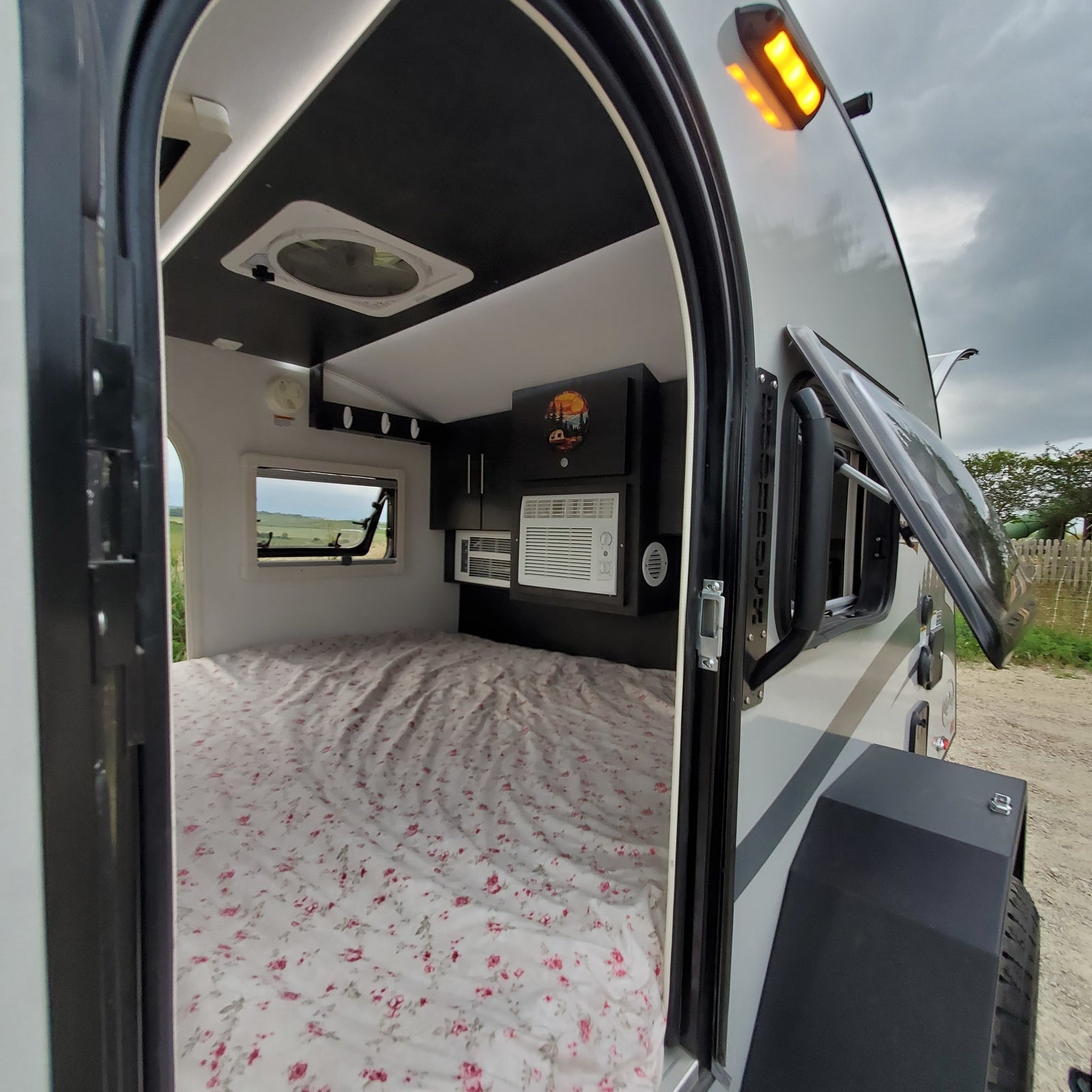 View of a compact rv rental interior with a floral-patterned bed, AC, and overhead cabinets, ideal for travel.