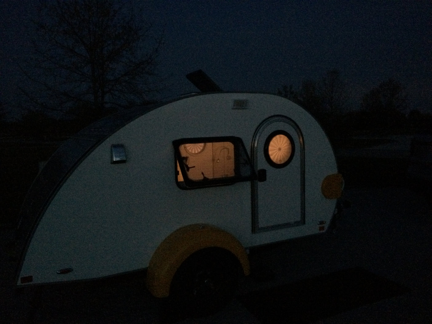 Teardrop rv rental glowing at night. Interior lights show a cozy space, perfect for an adventure.