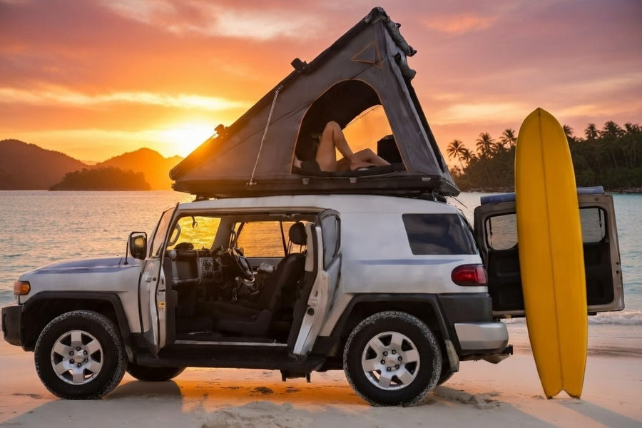Sunset beach camping in an RV rental SUV with a rooftop tent and surfboard.|A white SUV with a rooftop tent is parked on sandy terrain at sunset