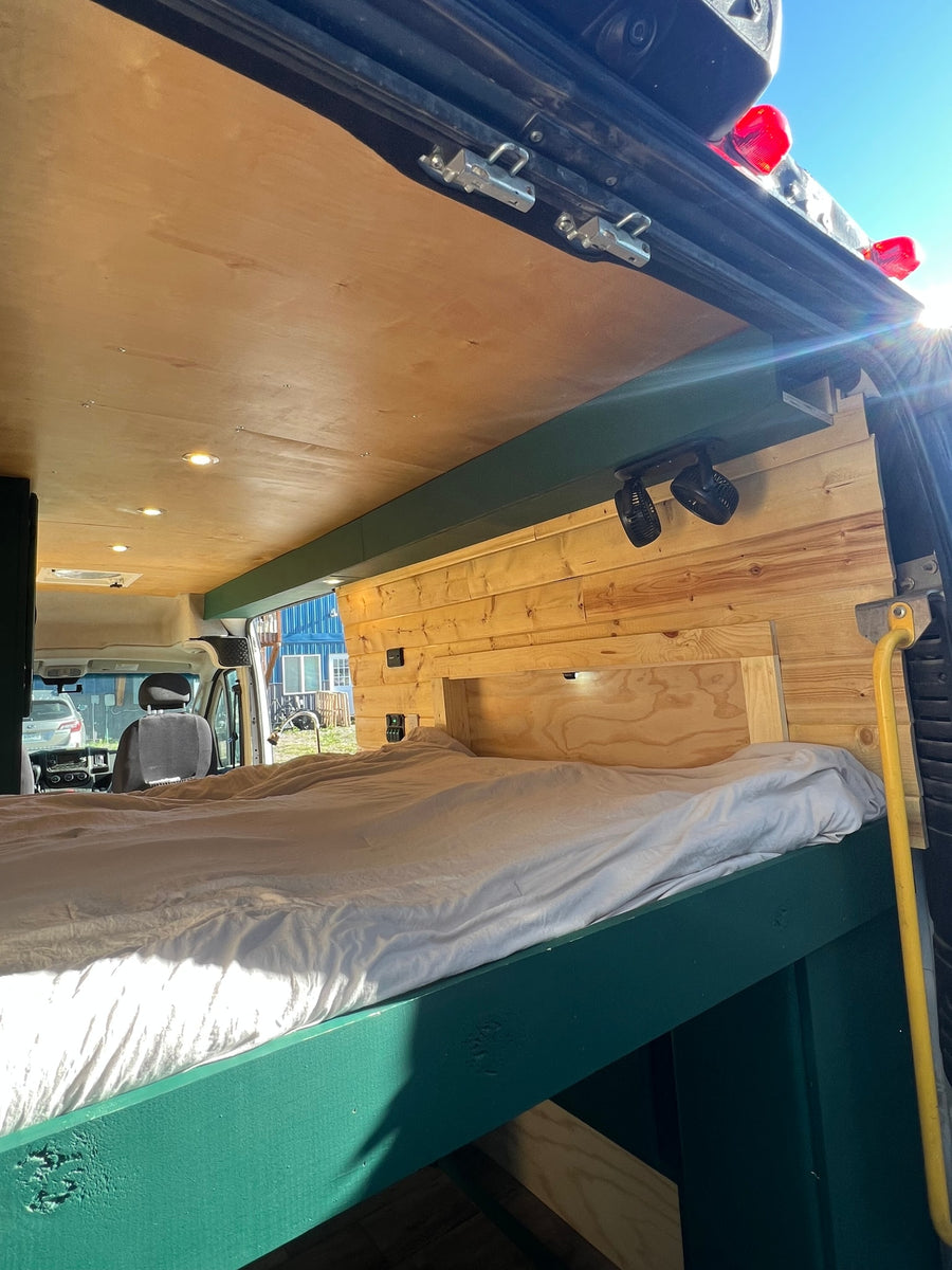 Cozy rv rental camper van interior. Features a custom wood bed, light wood-paneled walls, ceiling lights, and fans for comfort.