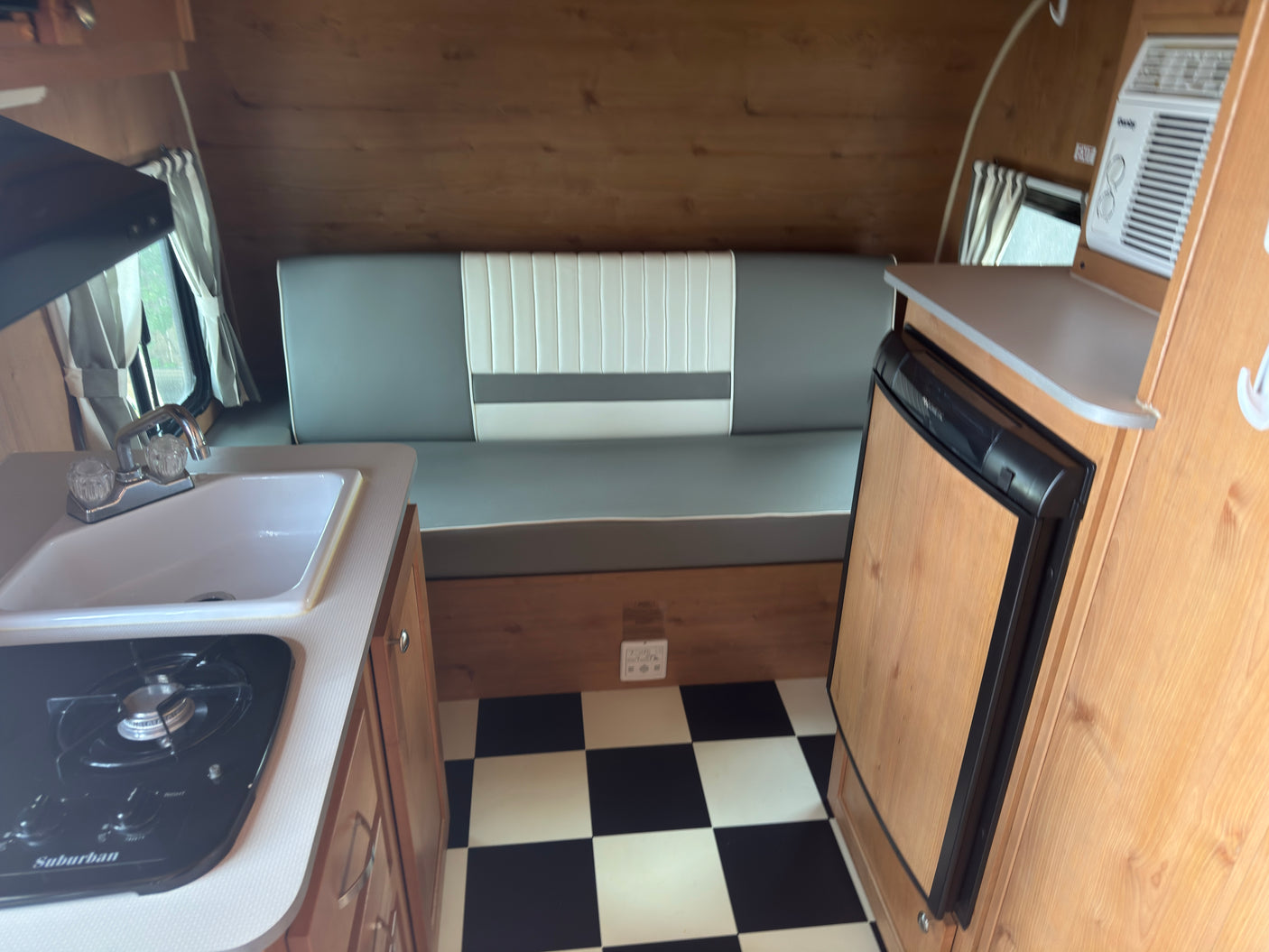 Retro RV rental interior features a compact kitchen with stove and sink, dinette seating, fridge, AC, and classic black-and-white checkered floor.