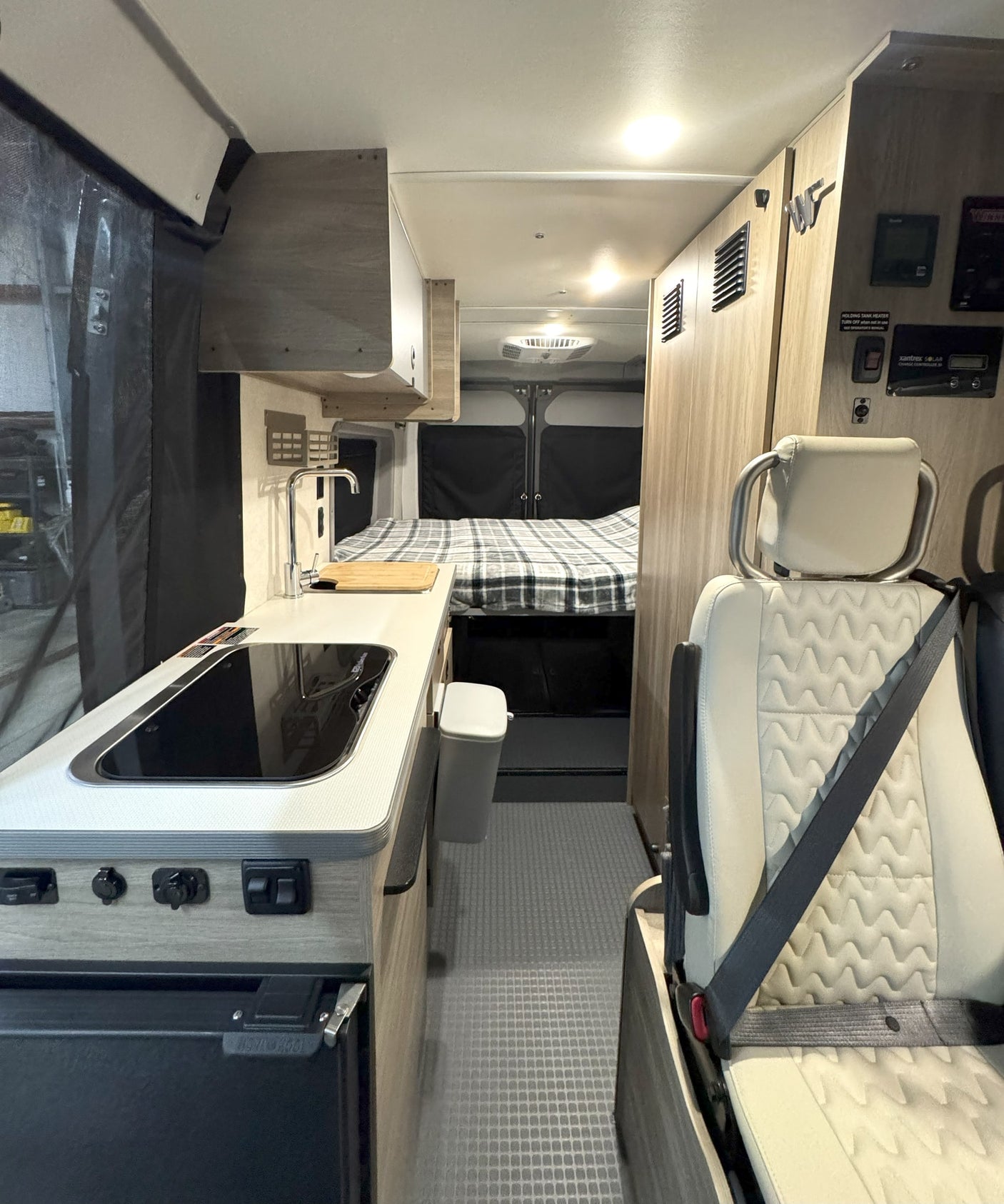 Clean rv rental interior: kitchen with sink/stovetop, cozy rear bed, and passenger seat, ready for adventure.