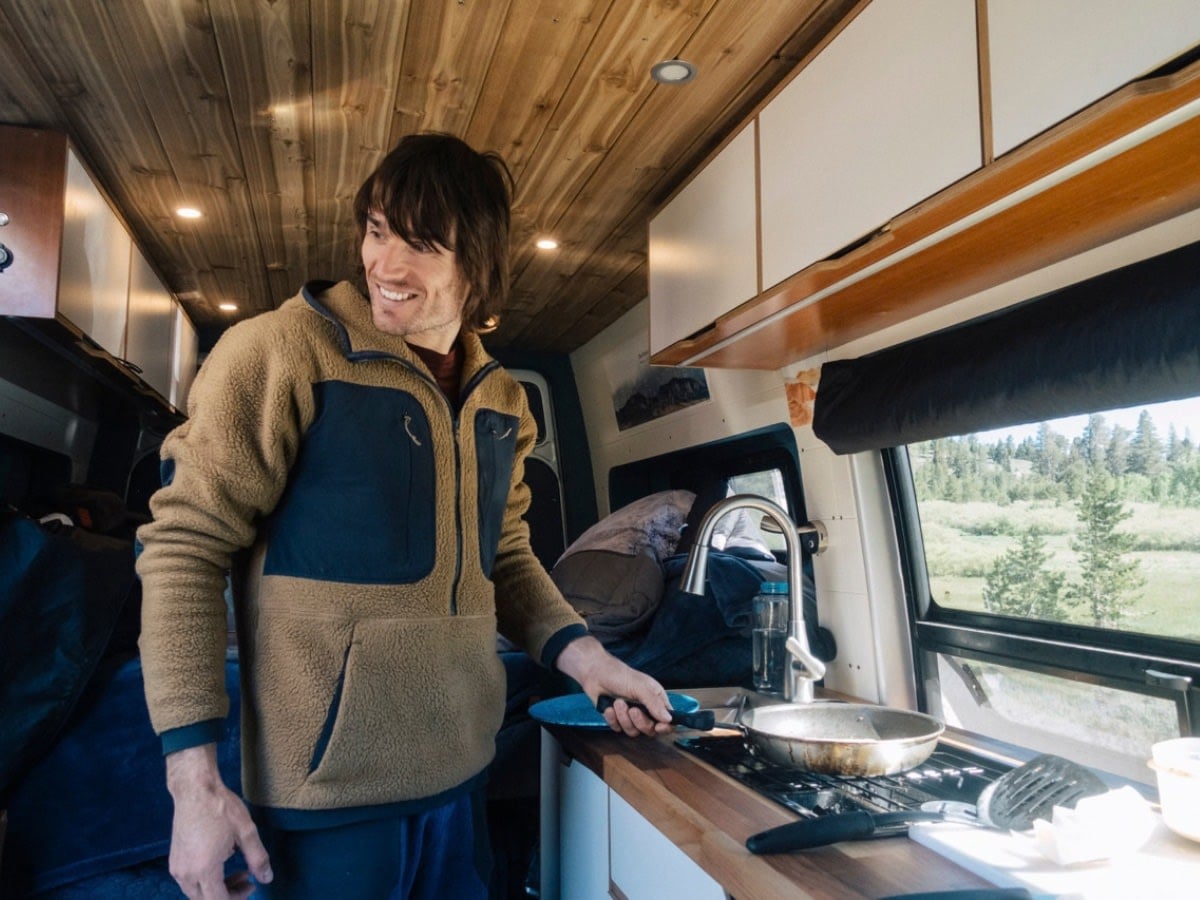 parked in a sunny forest setting.|Rv rental cooking: A man smiles while preparing food in his modern campervan kitchen — photo 2