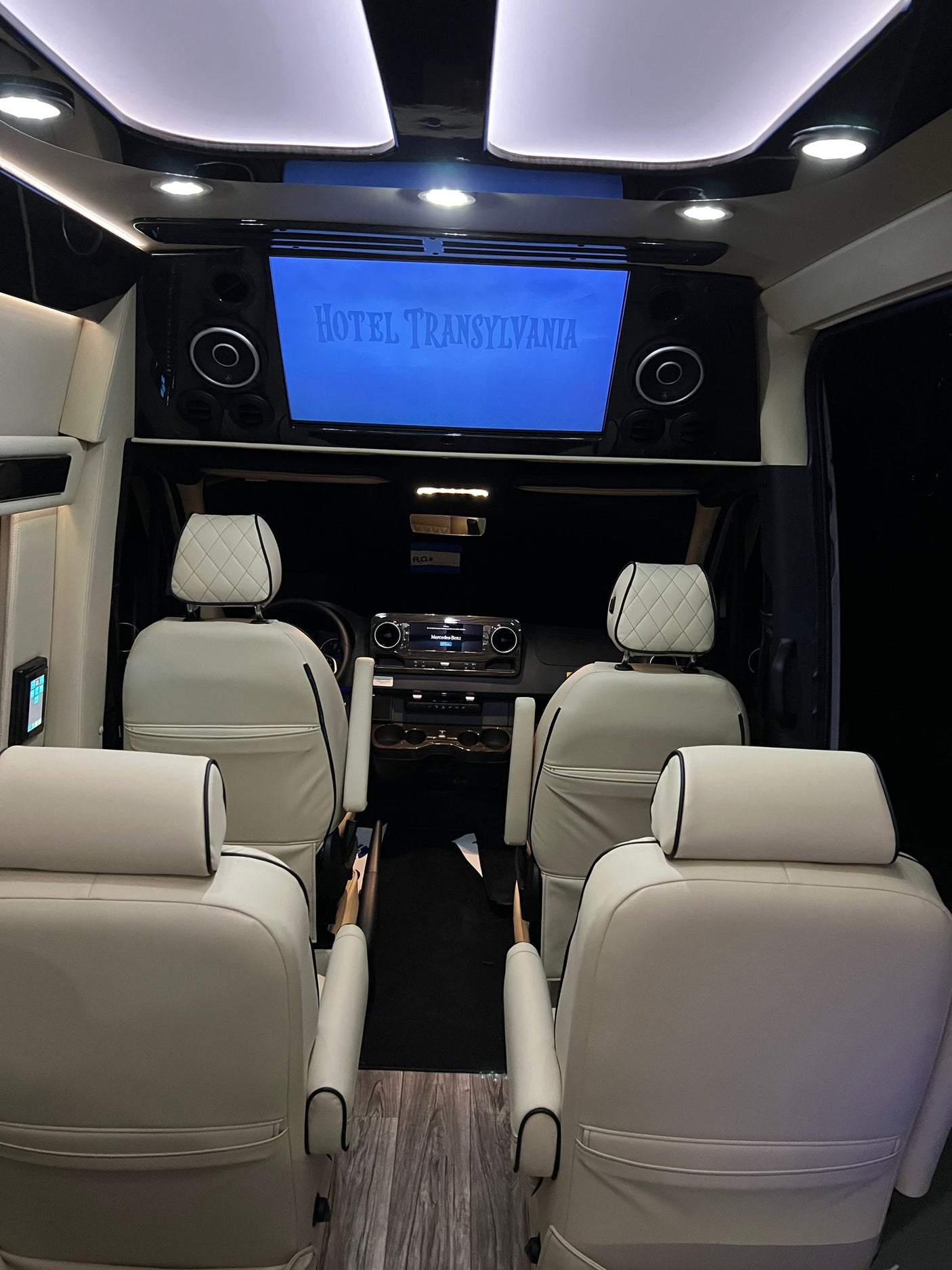 Luxurious RV rental interior with plush white seats & large screen playing "Hotel Transylvania." Perfect travel comfort.
