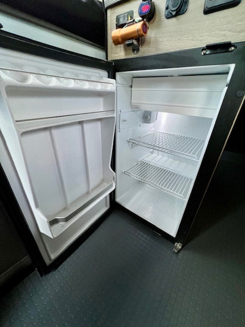 Open, empty mini-fridge inside an RV rental, showing wire shelves & door storage. Perfect for travel snacks.
