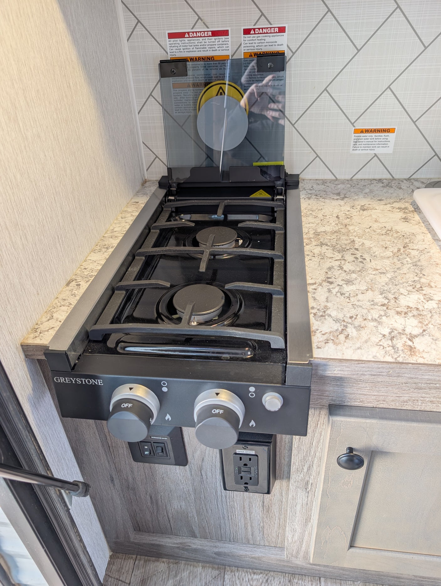 This RV rental kitchen features a Greystone gas stovetop with a glass cover, burner controls, and safety warnings for use.