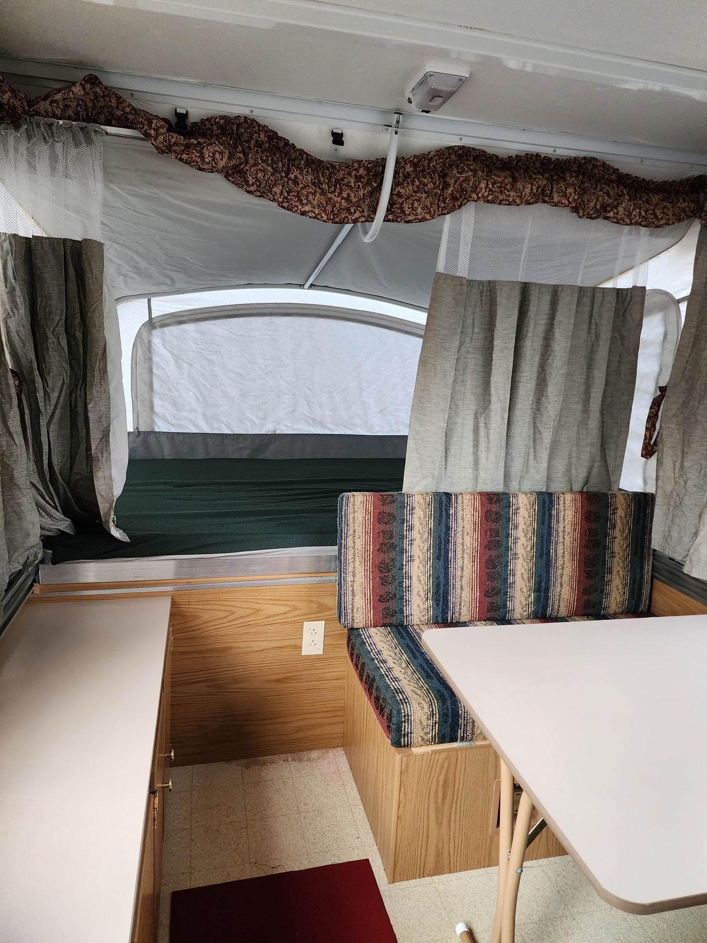 and bed area.|RV rental: Cozy pop-up camper dinette with striped cushions and a central table