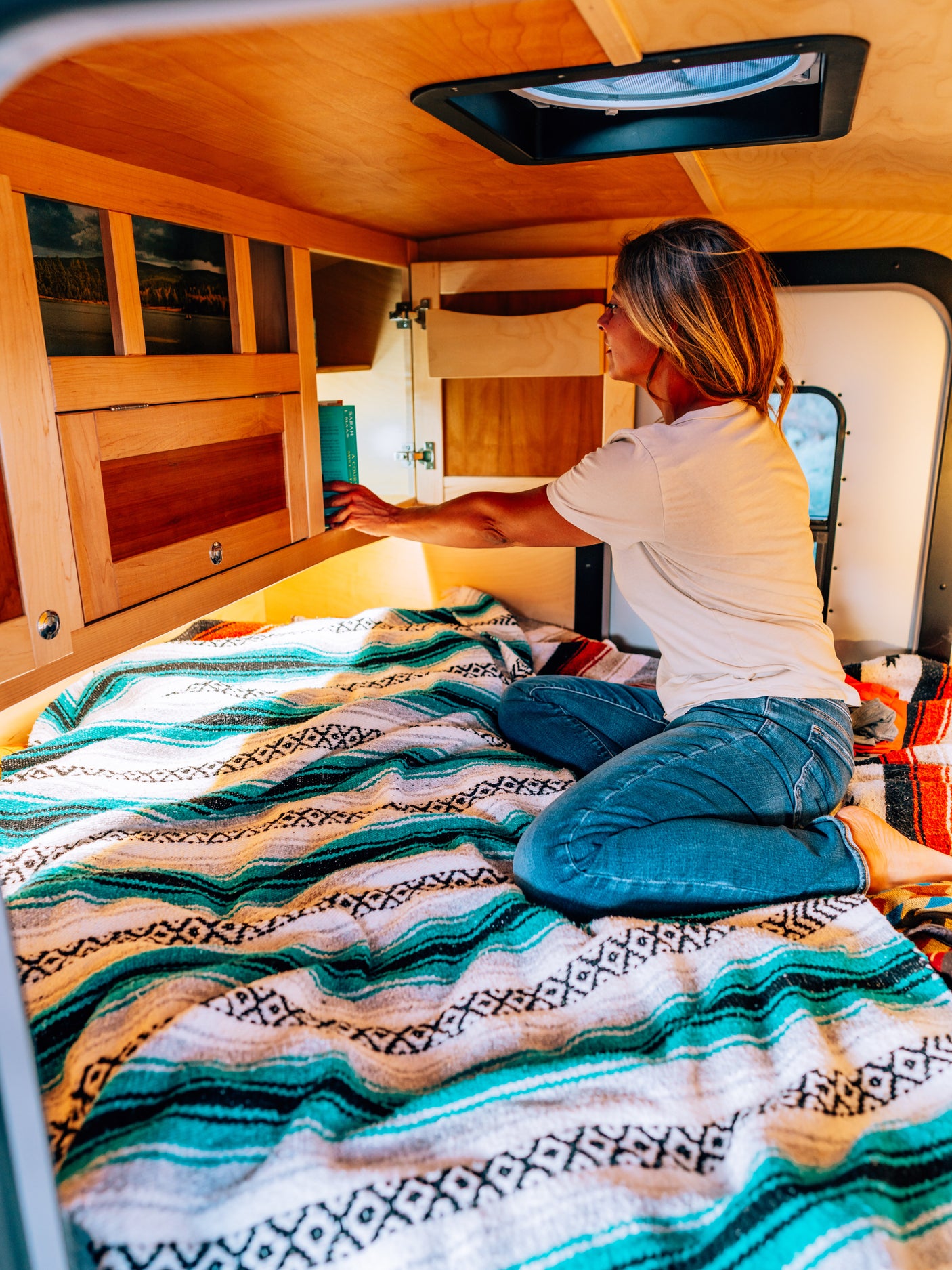 Woman finds a book in her cozy RV rental, sitting on a colorful patterned blanket. Perfect for mobile living.