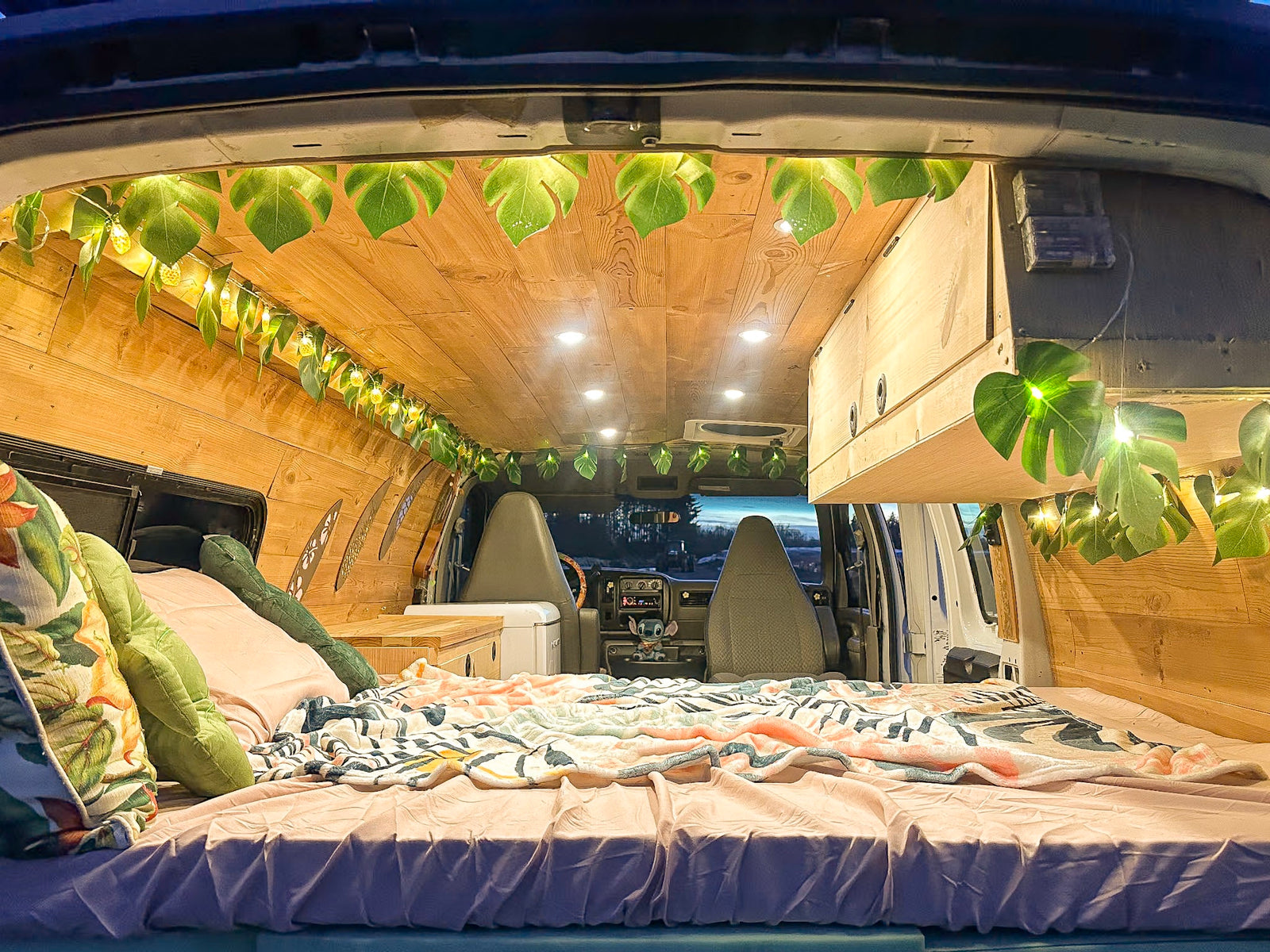 Experience **van life** in this cozy **RV rental**! A converted van with a comfy bed, wood walls, and ambient tropical leaf lights.