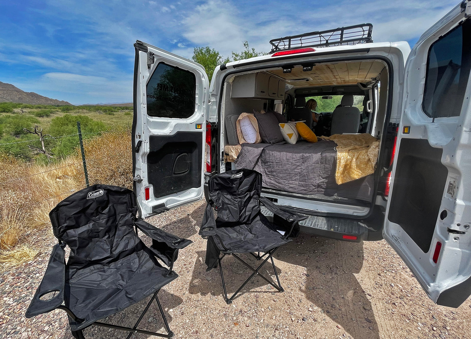 Your RV rental destination. Cozy camper van with bed and outdoor chairs setup for a peaceful camping experience in the desert.