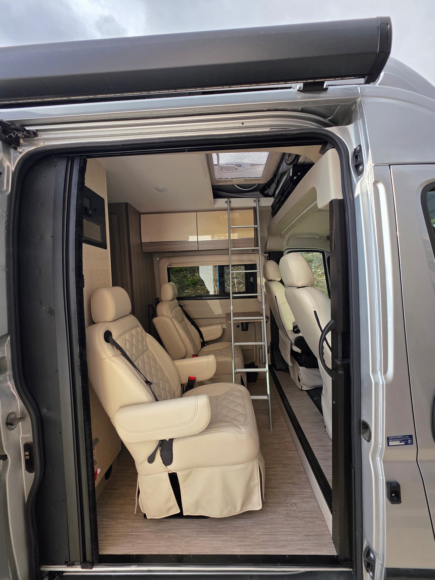 Spacious RV rental interior with comfy quilted seats, ladder to bunk, and modern design.