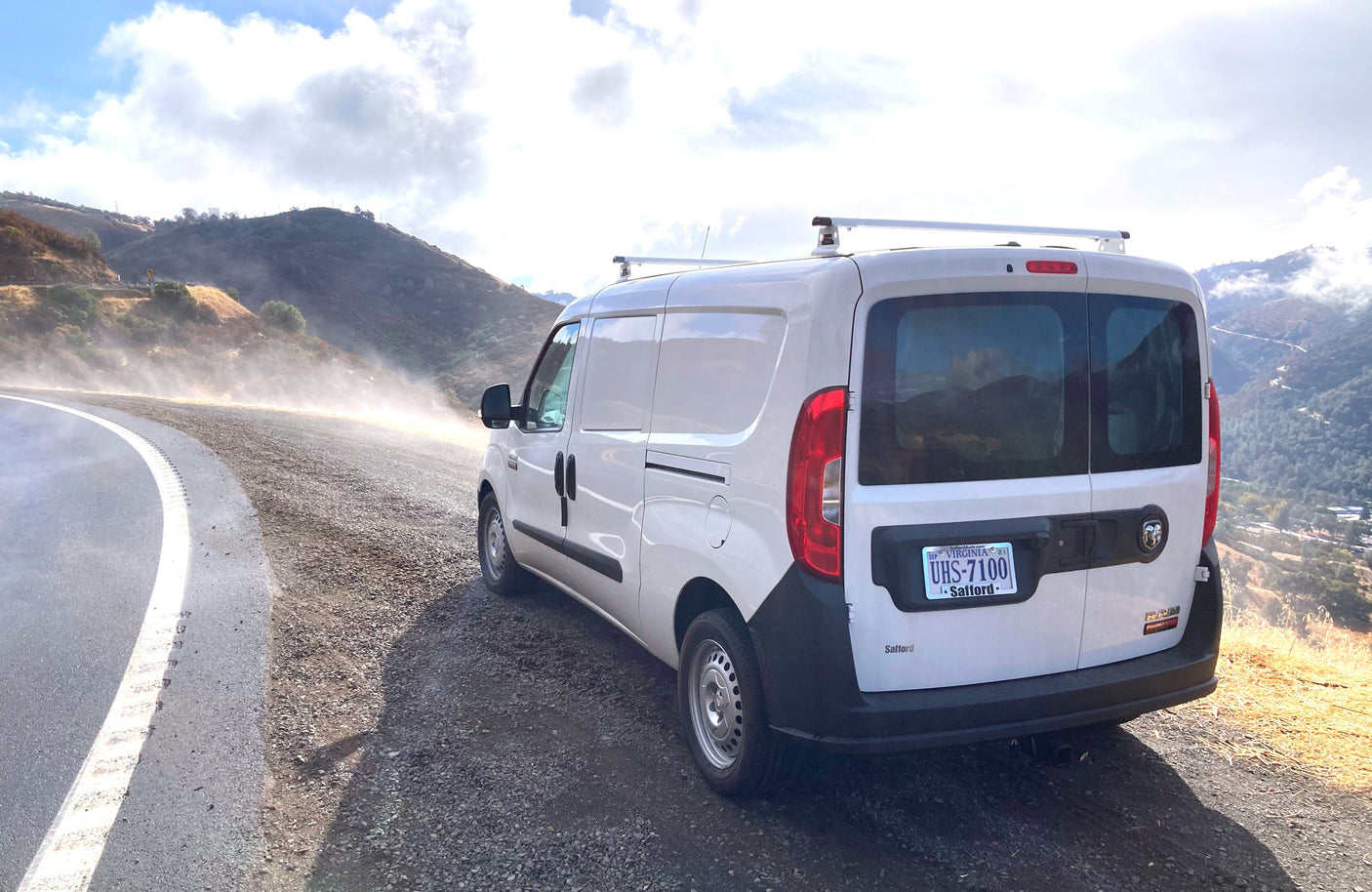 White Ram ProMaster City van with roof racks on a winding, misty mountain road. Perfect for adventure as an RV rental.