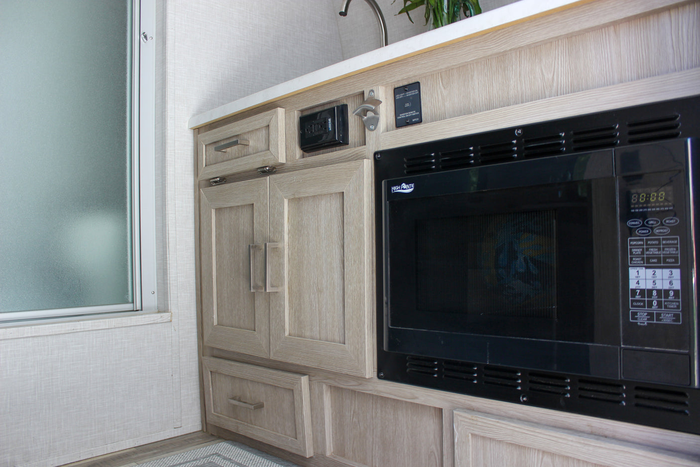 Clean RV rental kitchen area with High Pointe microwave, light wood cabinets, and frosted window.