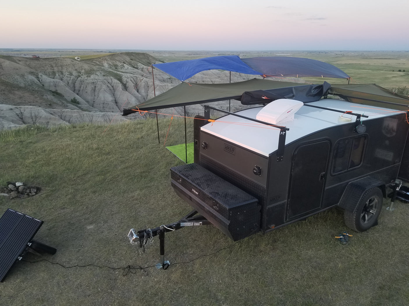 Teardrop trailer 'rv rental' at cliffside campsite with solar setup, overlooking badlands. Ideal for off-grid trips.
