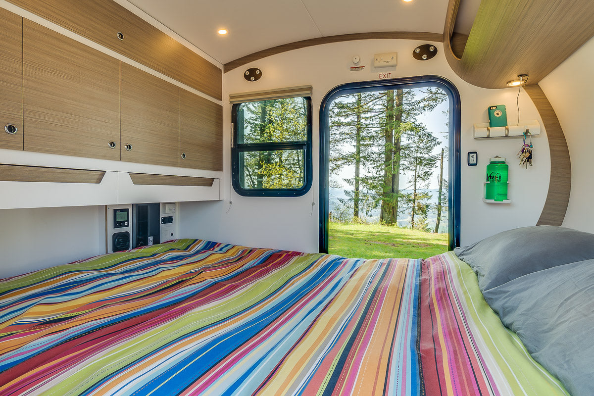 This RV rental offers a compact, cozy bedroom with overhead storage & a view of pine trees. Perfect for adventure!