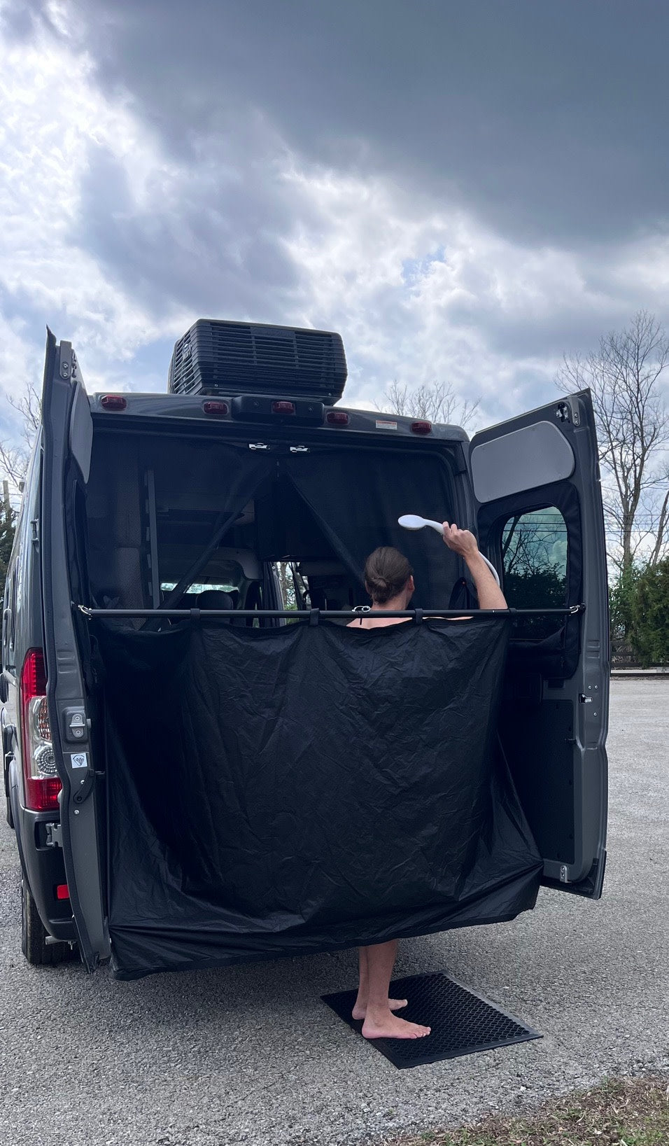 RV rental van with rear outdoor shower setup. Person uses a privacy curtain and handheld shower on a mat.
