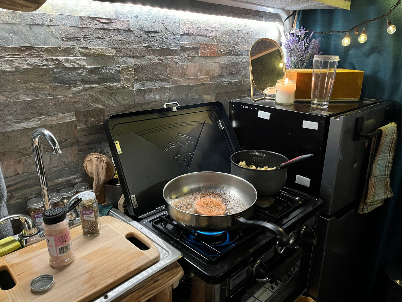 This compact RV rental kitchen features a gas stove cooking a meal, with a sink and spices ready for adventure.