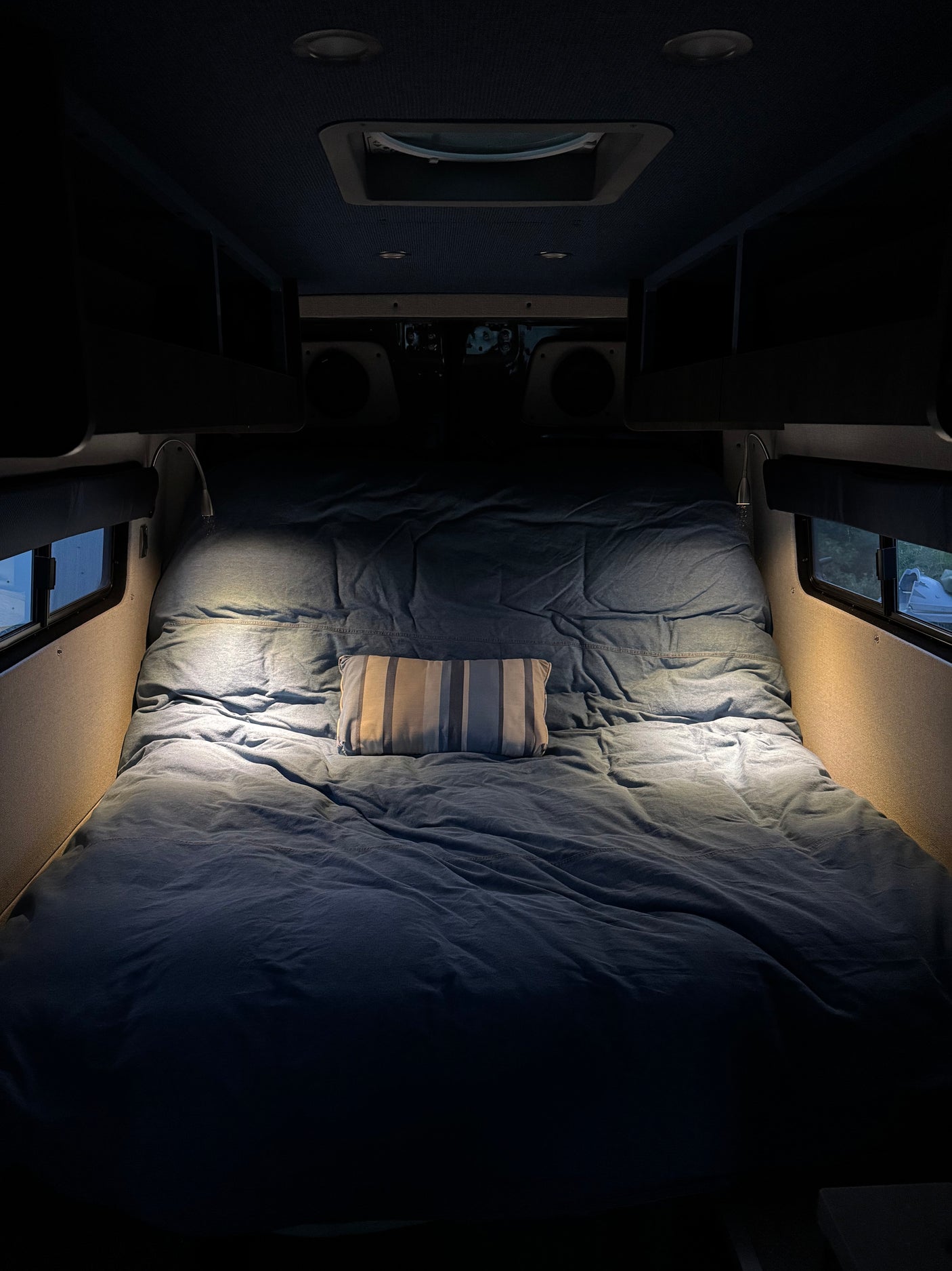 This RV rental's cozy bed features denim-blue bedding, a striped pillow, and bright reading lights for comfortable travels.