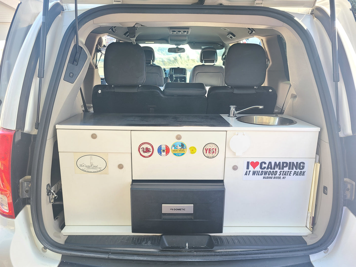Custom camper van conversion, ideal for RV rental, featuring a compact kitchen with sink, fridge, and storage for trips.