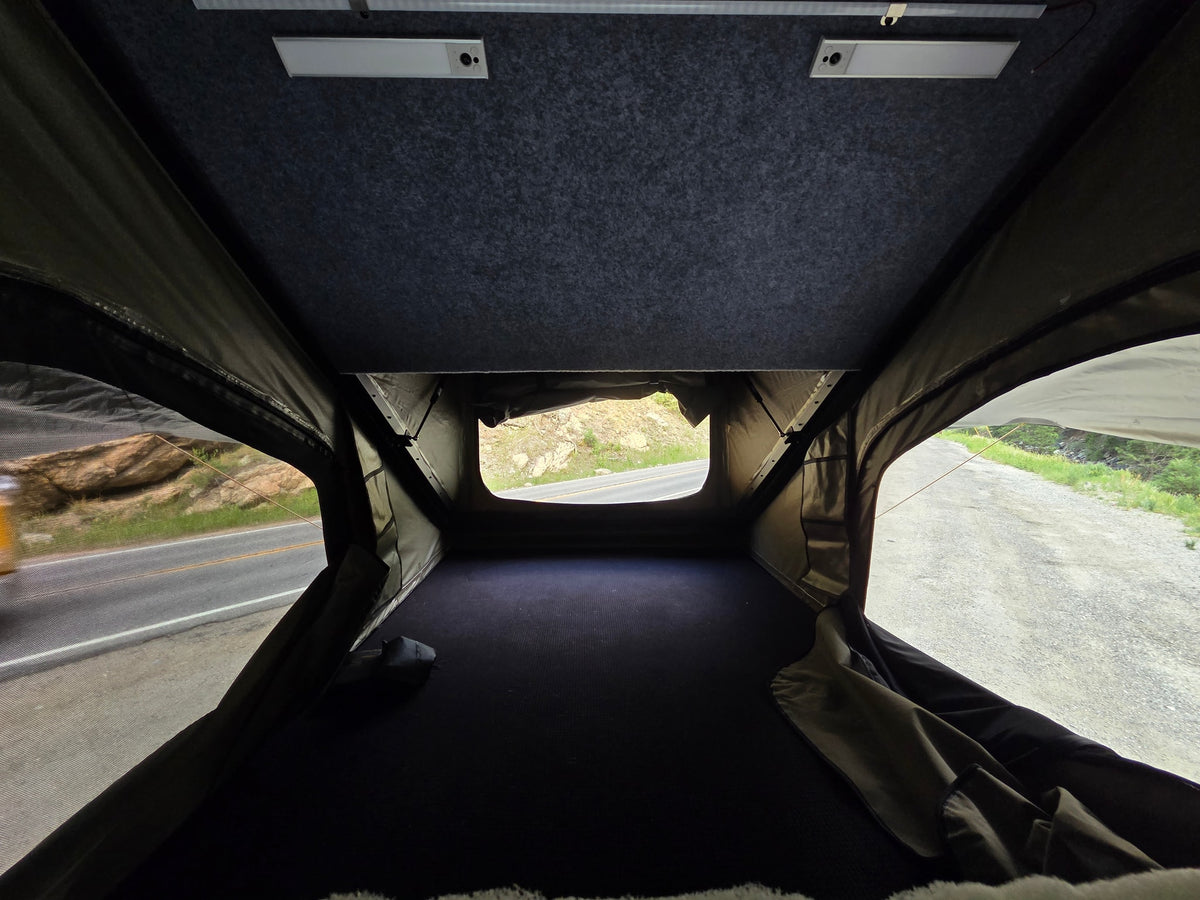 Cozy rv rental rooftop tent interior with a dark bed, overhead lights, and a roadside view for your next adventure. — photo 10