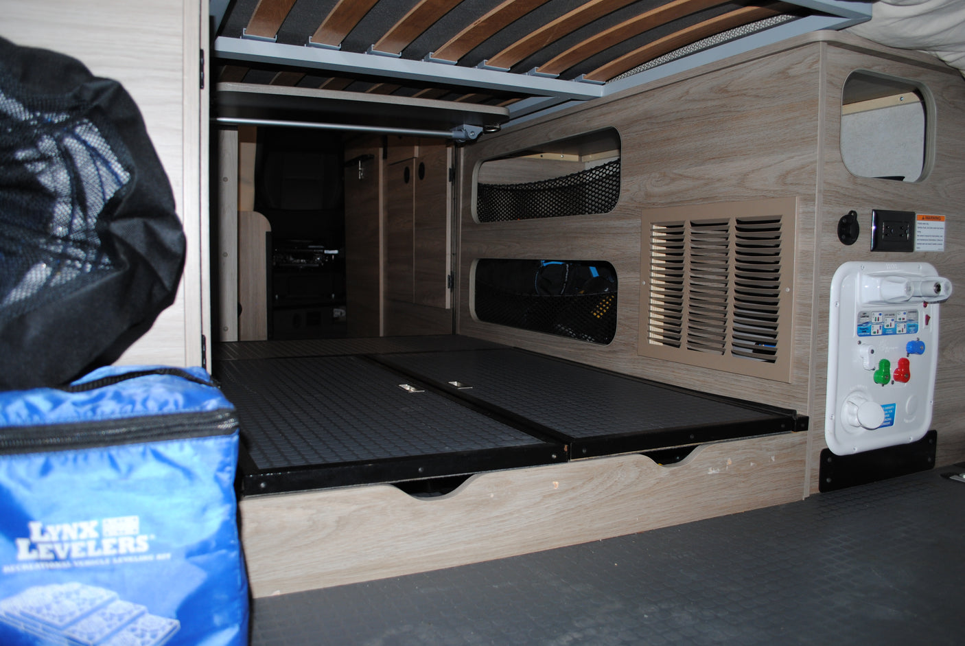 RV rental rear storage area features utility panel (water/electric), vented interior, and bed frame above.