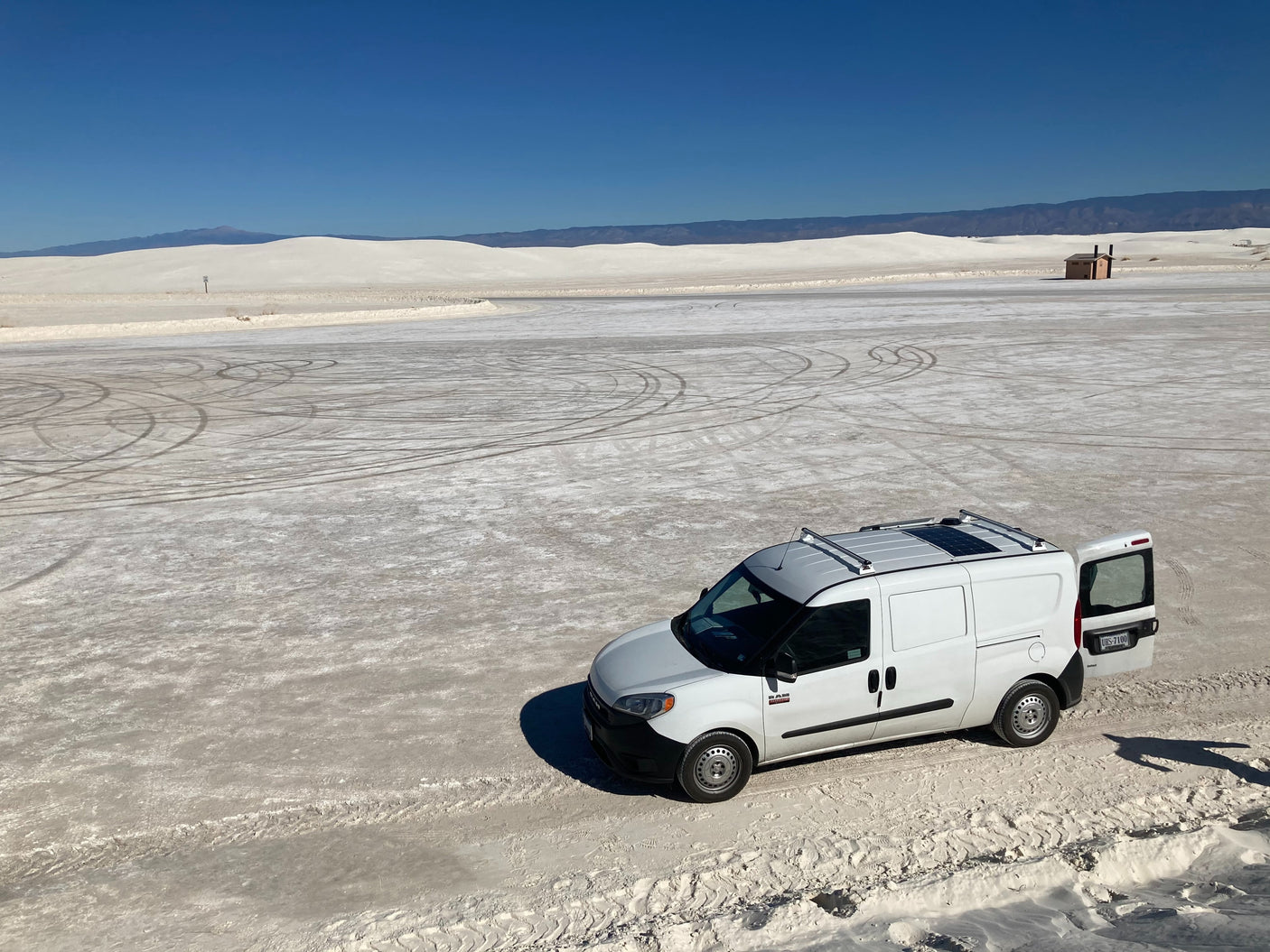 White Sands National Park: An RV rental van with an open rear door stands on vast white gypsum sands under a clear sky.