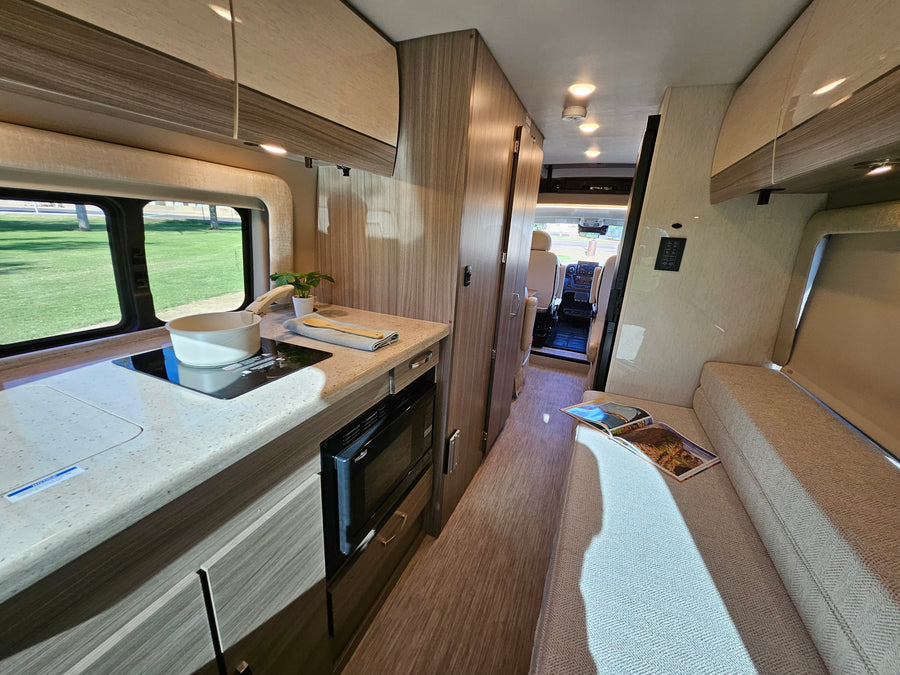 Modern RV rental interior with a compact kitchen, lounge seating, and a view to the outside, ideal for road trips.