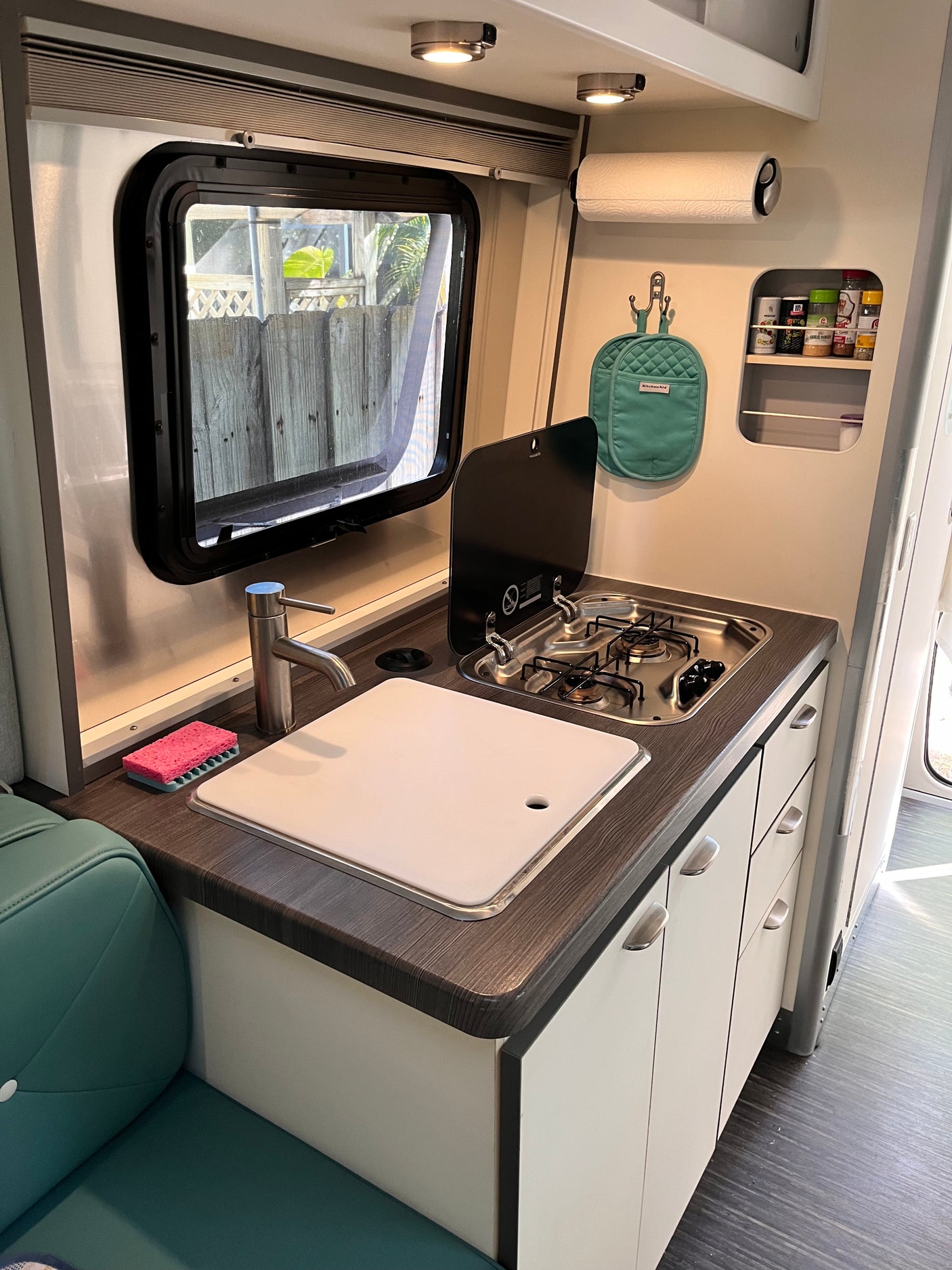 Compact RV rental kitchen features a sink, stove, and cutting board, perfect for on-the-road meals.