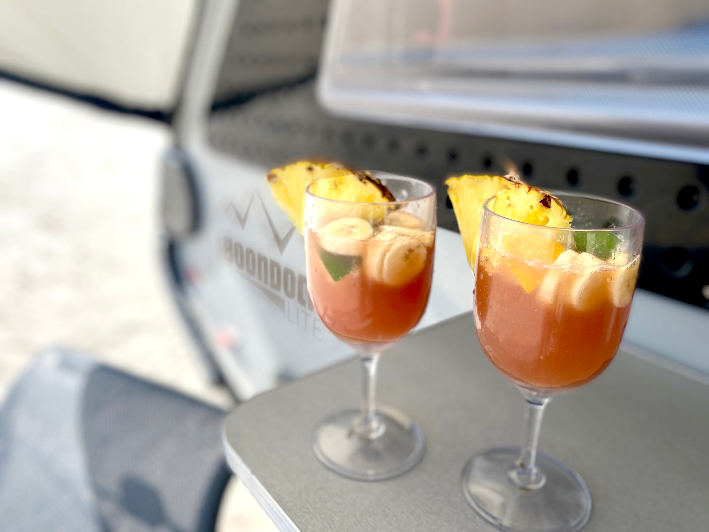 Two refreshing fruit drinks with pineapple and banana sit on a table outside an RV rental. Perfect travel treat.