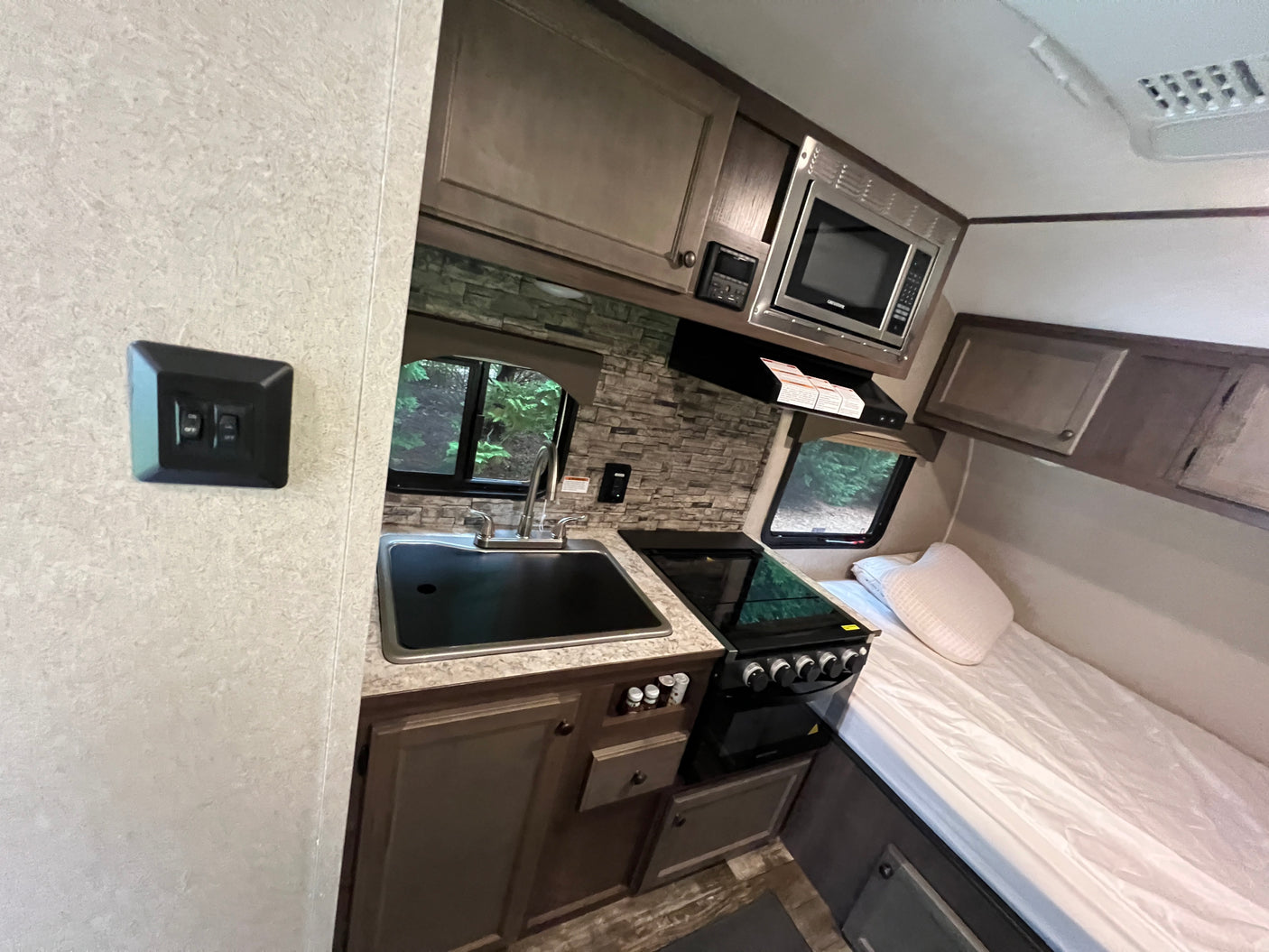 RV rental interior showcasing a compact kitchen area with a sink, stove, microwave, and an adjacent bed.