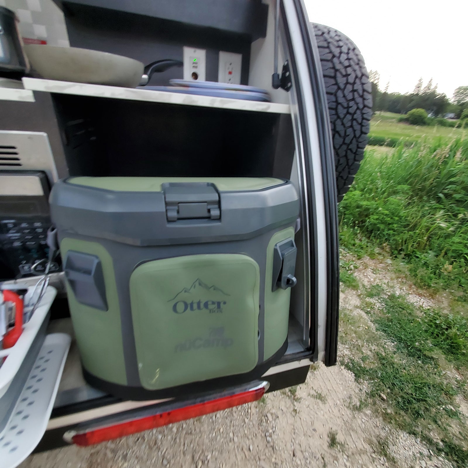 Compact outdoor kitchen of an rv rental, showing a nuCamp camper with an Otter cooler, cooking pan, and electrical outlets for camp life.