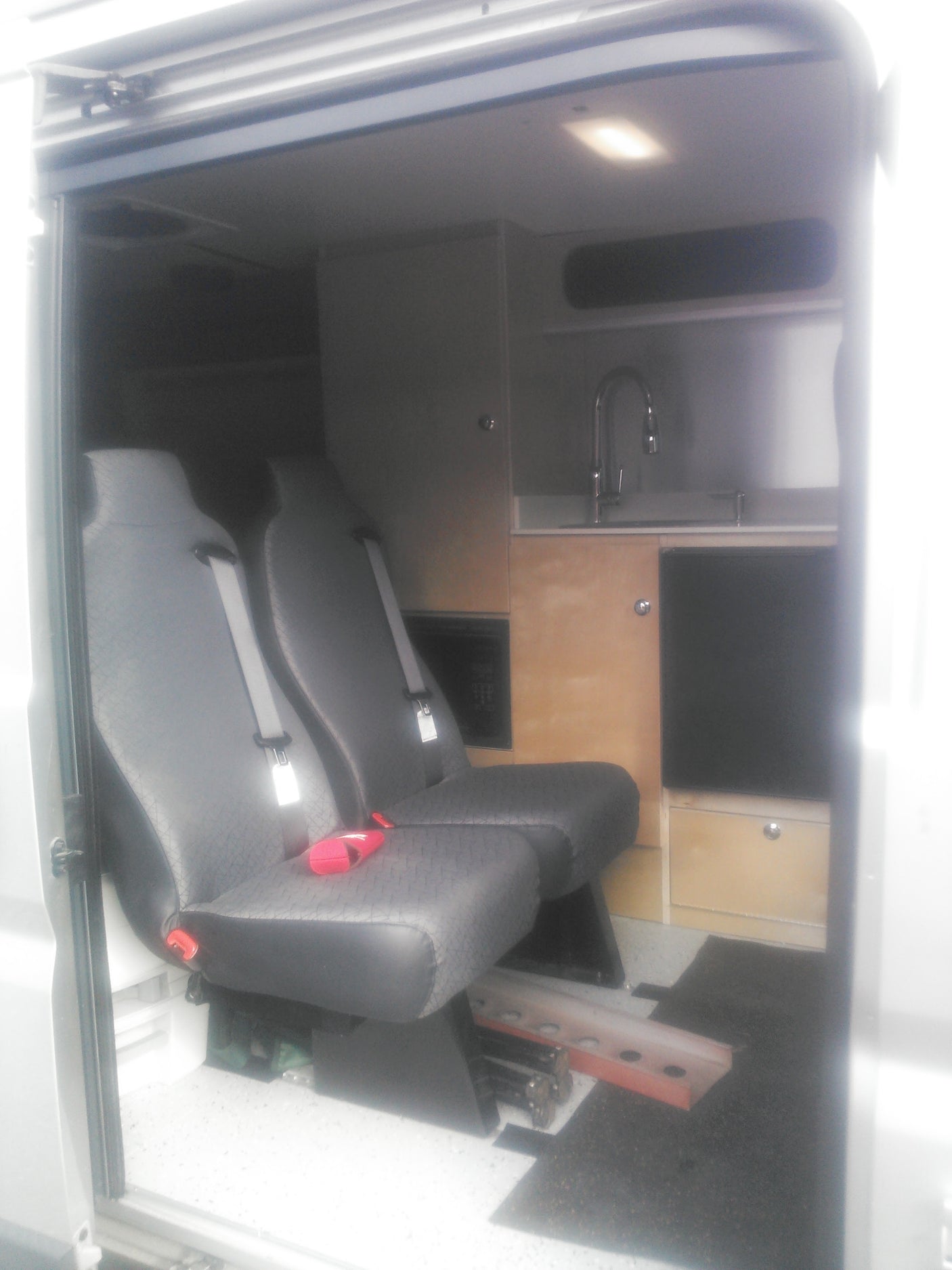 RV rental interior: comfy grey seats, a compact kitchen with sink, and wooden cabinets for cozy camper travel.