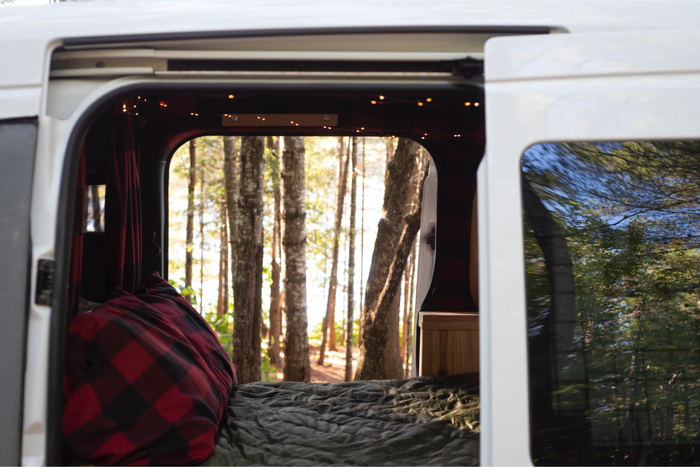 Cozy RV rental camper van interior with string lights, looking out to a sunlit forest. Perfect for nature adventures.