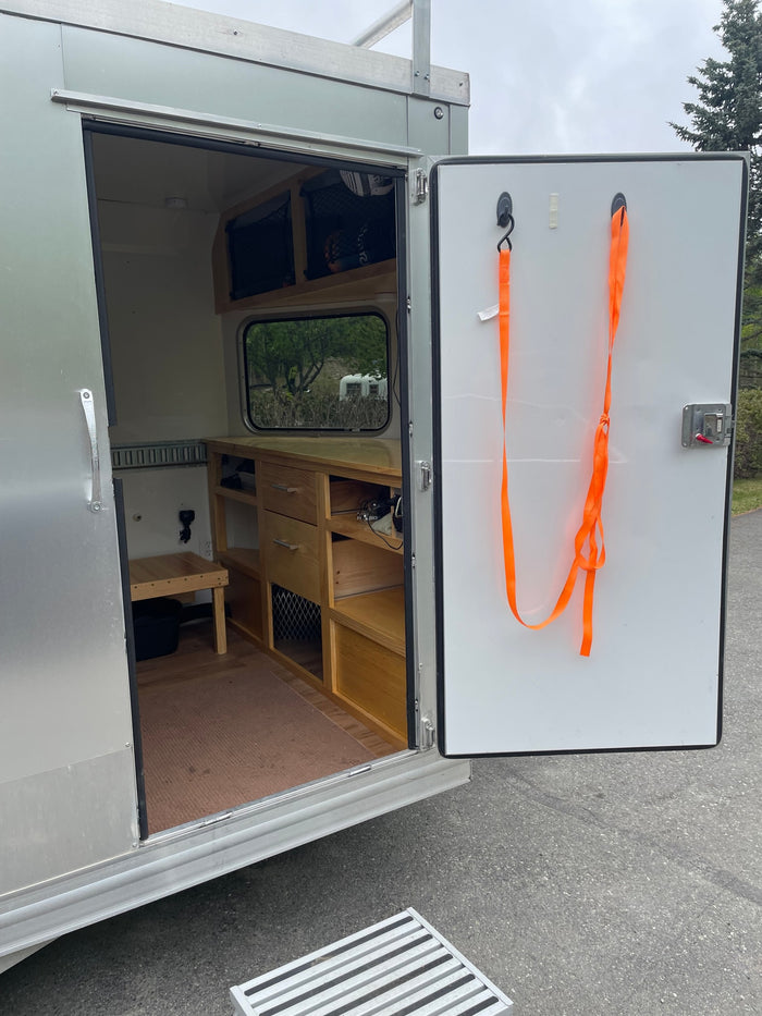 Open door of an RV rental showing custom wood interior, storage, and a view outside. Mobile living.