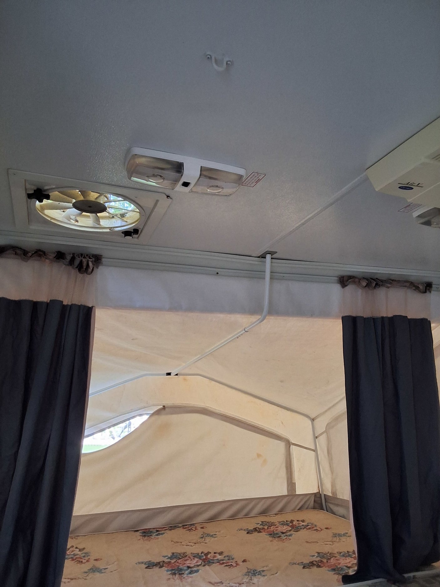 Interior of an RV rental, featuring a ceiling fan, lights, support structure, privacy curtains, and a bed with floral bedding.