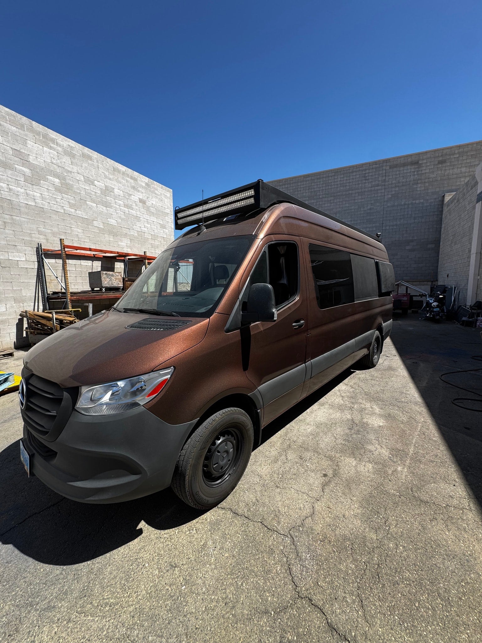 Customized brown Mercedes Sprinter van with a roof light bar, ready for RV rental adventures under blue skies.