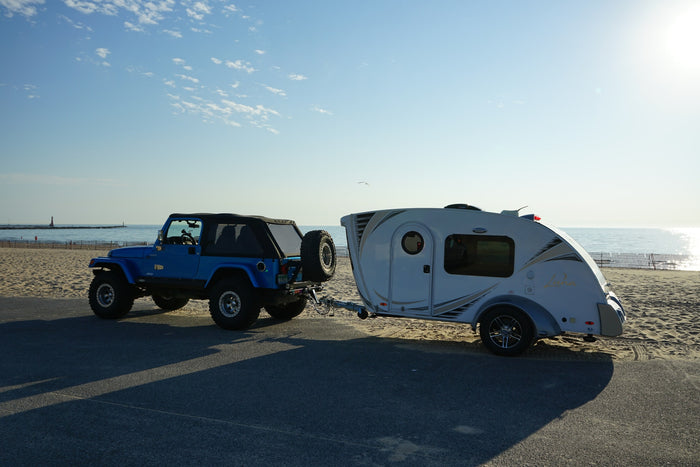 chairs ready for relaxing camp vibes.|Blue Jeep tows a white teardrop trailer by a sandy beach. Ideal for an RV rental getaway near the ocean!|An RV rental kitchen with a sleek