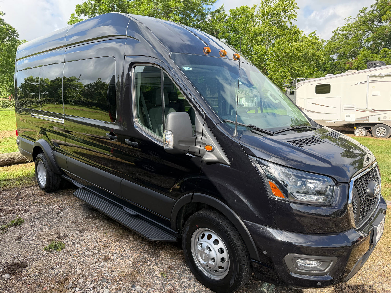 Stylish black Ford Transit van, suitable for rv rental adventures, parked near a white RV amidst trees.